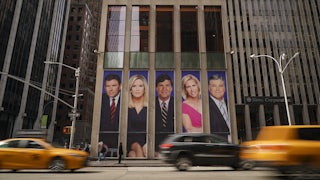 Fox News host photos on billboard on giant building in New York. Cars drive by in front.