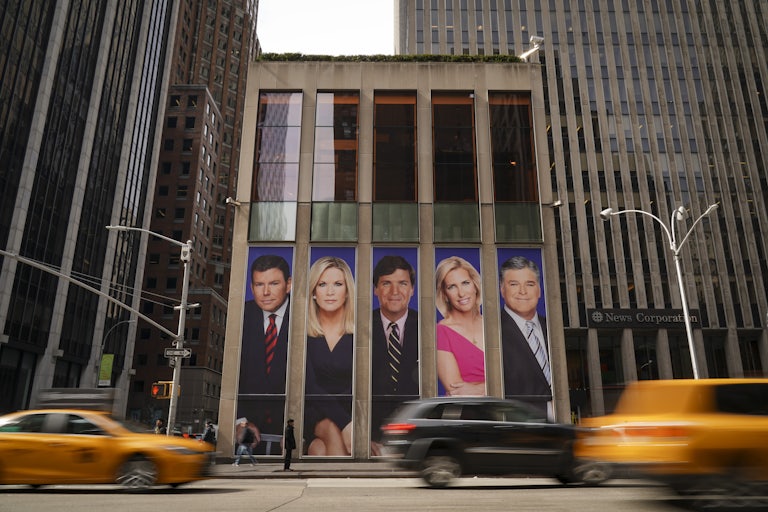 Fox News host photos on billboard on giant building in New York. Cars drive by in front.