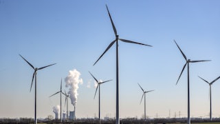 Coal plant towers steam behind wind turbines in the foreground.