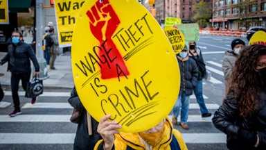 A New York City laundromat worker hold up a yellow sign that says "Wage Theft Is a Crime" during a protest in November 2020.