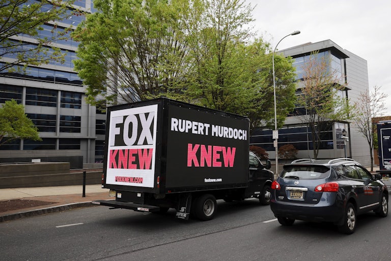 A truck with a digital sign saying, "RUPERT MURDOCH KNEW" and "FOX KNEW" drives on the road. On the sign is also the website "foxknew.com."