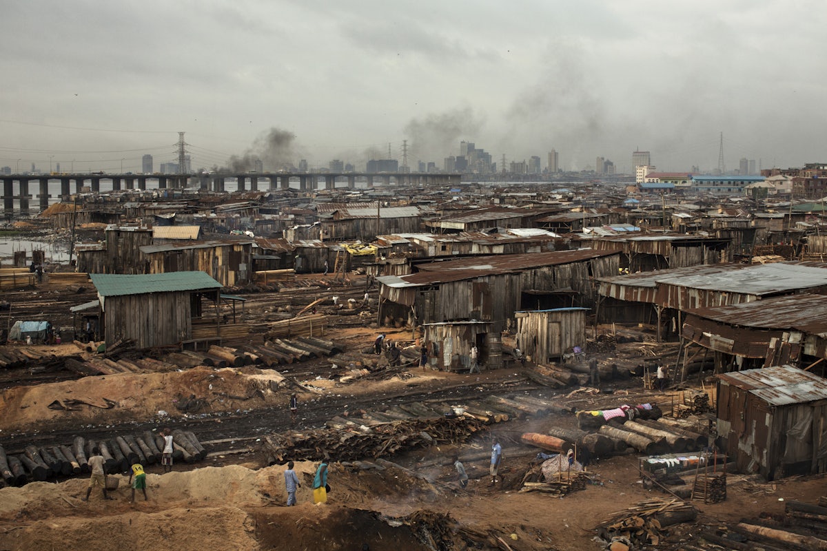 Smoke billows from logs covered with soil next to sheds in Lagos.
