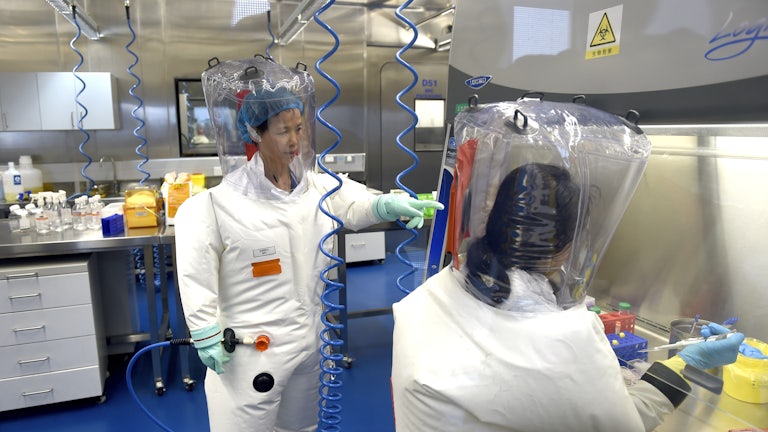 Two researchers in protective gear work in a lab.