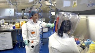 Two researchers in protective gear work in a lab.