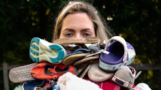 A tired mom carries a huge pile of laundry that almost covers her face. The title is Optimizes Efficiency from the series “Résumé of a Stay at Home Mom” by