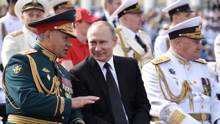 President Putin sits, smiling, between Russia's defence minister and the commander in chief of the Russian Navy, in 2017.