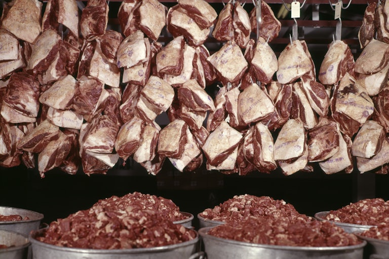 Cuts of raw beef hang from the ceiling with tins of chopped beef below.