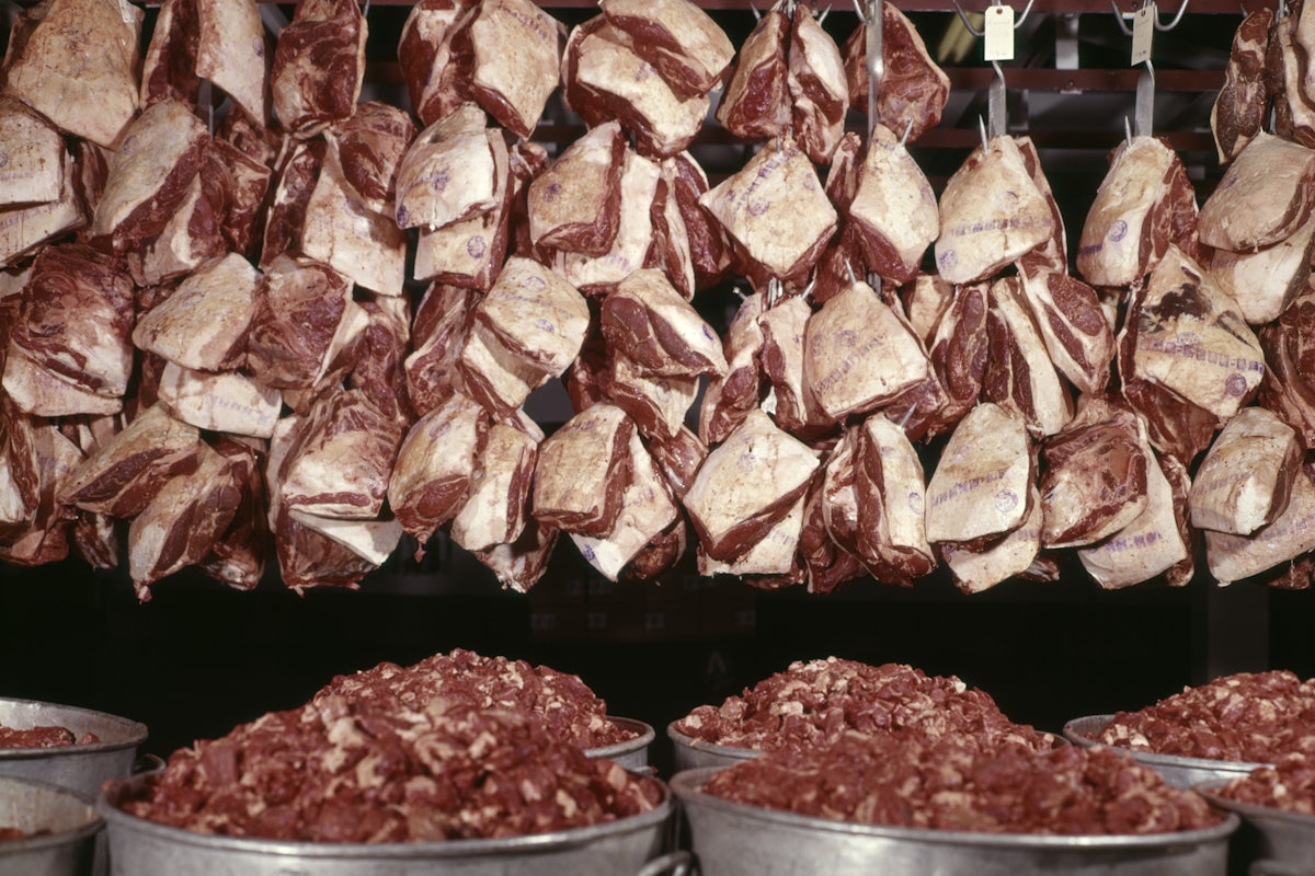 Cuts of raw beef hang from the ceiling with tins of chopped beef below.