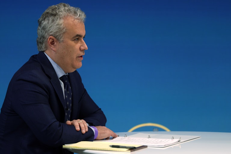 Jeffrey Zients sits at a table with a binder, notepad, and pen in front of him (right profile shot)