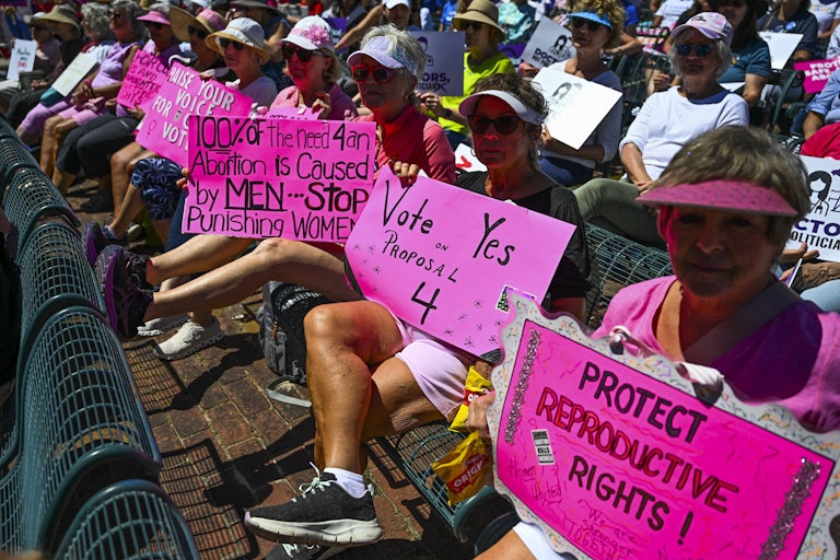 People hold up protest signs in support of Florida’s abortion amendment initiative