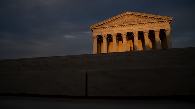 The facade of the U.S. Supreme Court lit by a setting sun, foregrounded by shadows.