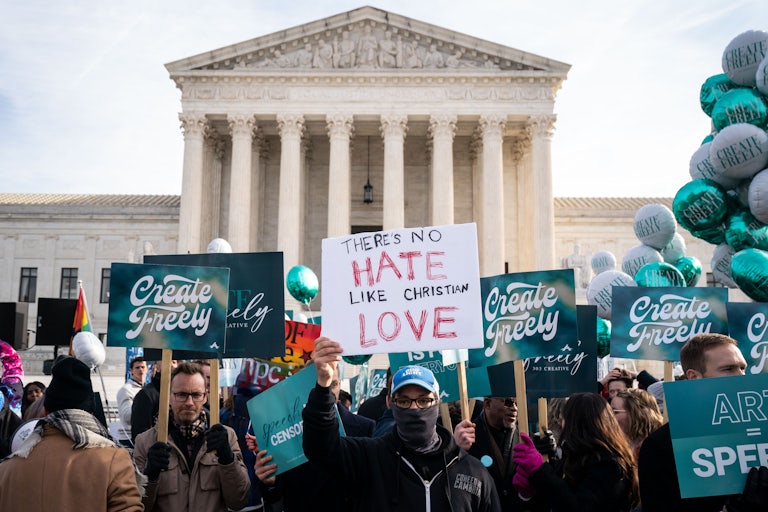 A crowd of protesters gather in front of the Supreme Court building. One protester holds up a sign that says THERE'S NO HATE LIKE CHRISTIAN LOVE, while others hold up signs that say CREATE FREELY.