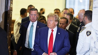 Donald Trump in the courtroom. Others stand around him, including his legal team and a security guard.