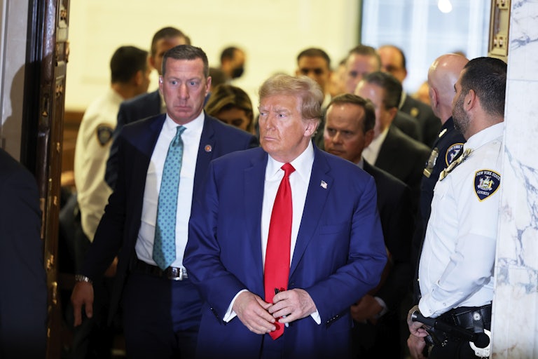 Donald Trump in the courtroom. Others stand around him, including his legal team and a security guard.