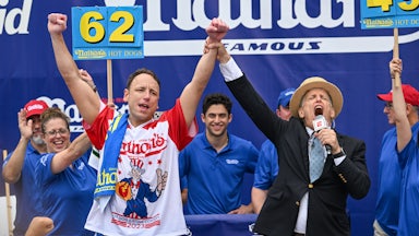 Joey Chestnut raises his hands as an announcer clasps his wrist.