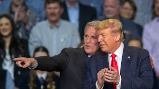 Kevin McCarthy wraps his arm around Donald Trump's shoulders and points off into the distance. They both smile. Trump is clapping. A crowd is in the background