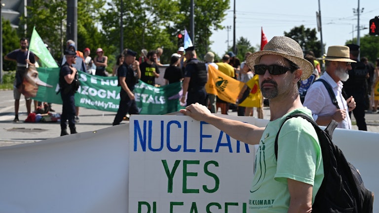 A pro-nuclear demonstrator holds a sign reading "NUCLEAR YES PLEASE!"