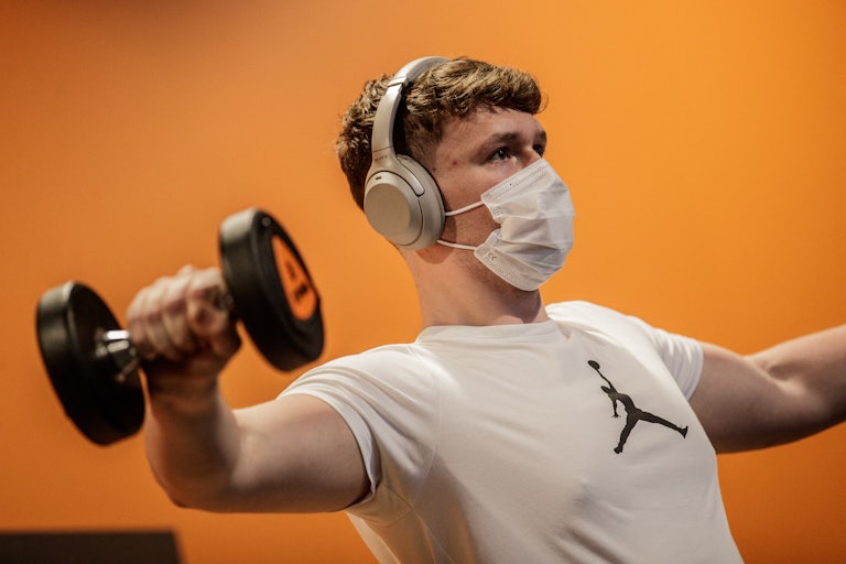 A person lifts weights in a gym while wearing a Covid face mask 
