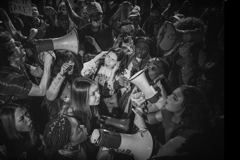 Screenshot of the Super Bowl Jesus ad; a bunch of young people yelling at each other via megaphones (black and white photo)