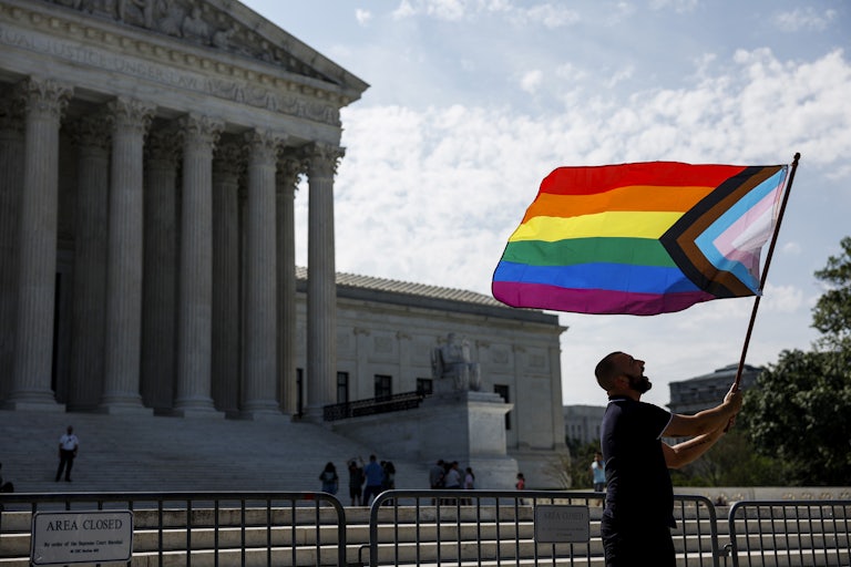 Someone waves a Pride flag in front of the Supreme Court