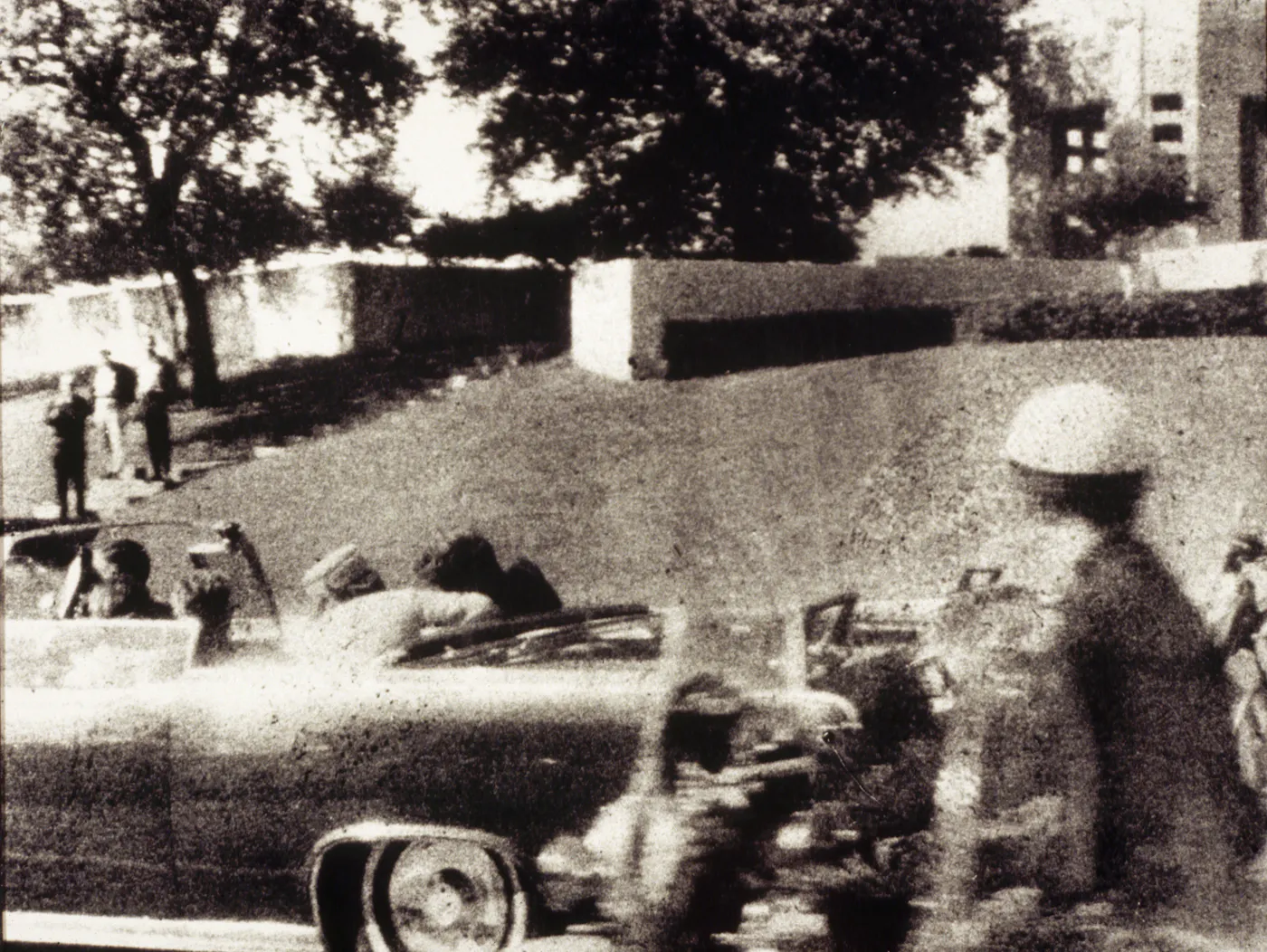 A grainy black-and-white photograph of the presidential motorcade at the moment of President Kennedy's assassination in in Dallas, November 22, 1963.