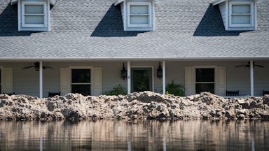 A levee holds back water in front of a house.