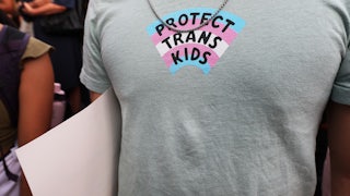 A close-up of someone's T-shirt, which has a trans flag with the text "Protect Trans Kids."