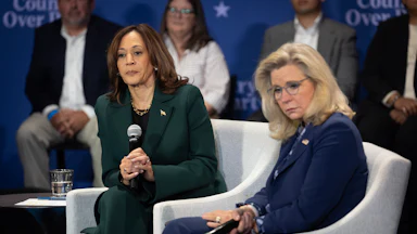 Kamala Harris and Liz Cheney seated on two chairs looking grim