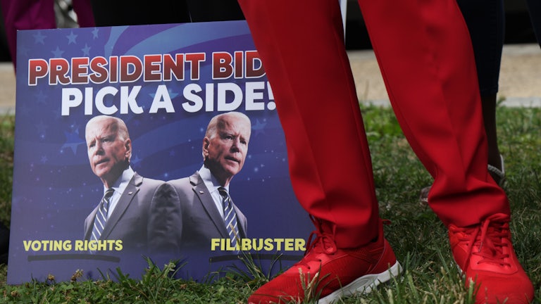 A man in red slacks stands next to a sign urging President Joe Biden to fight for the right to vote.