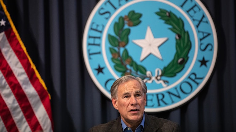 Texas Governor Greg Abbott sits in front of the Texas State Seal.