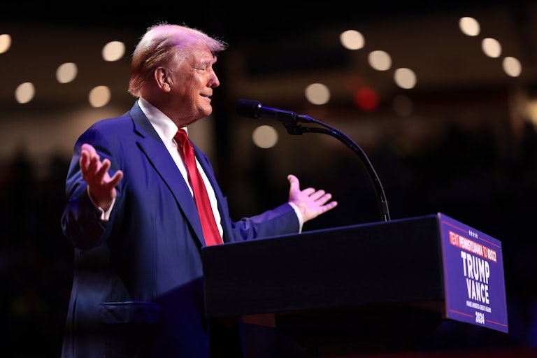 Donald Trump smiles and holds his arms out while standing at a podium during a campaign rally