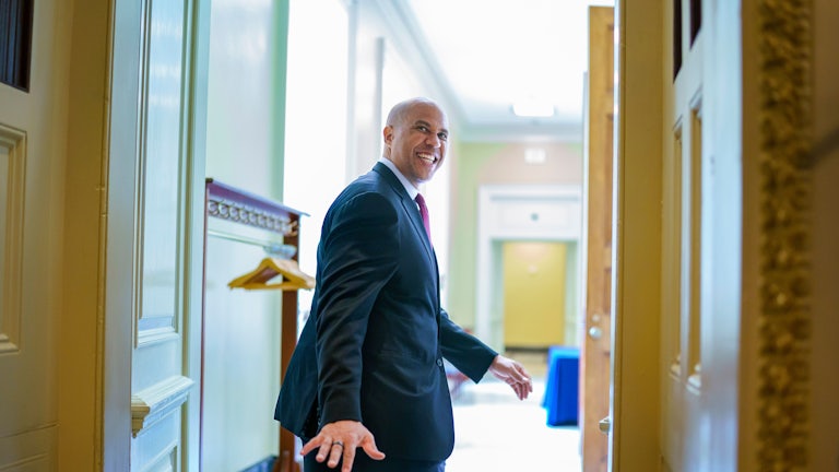 A smiling Senator Cory Booker looks back to wave goodbye as he leaves a room.