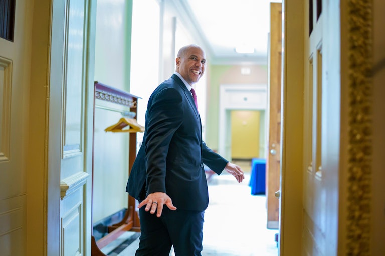 A smiling Senator Cory Booker looks back to wave goodbye as he leaves a room.