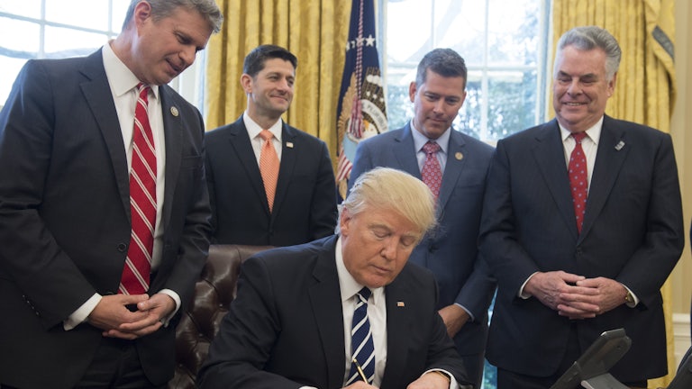 Donald Trump signs a piece of paper at his desk in the Oval Office