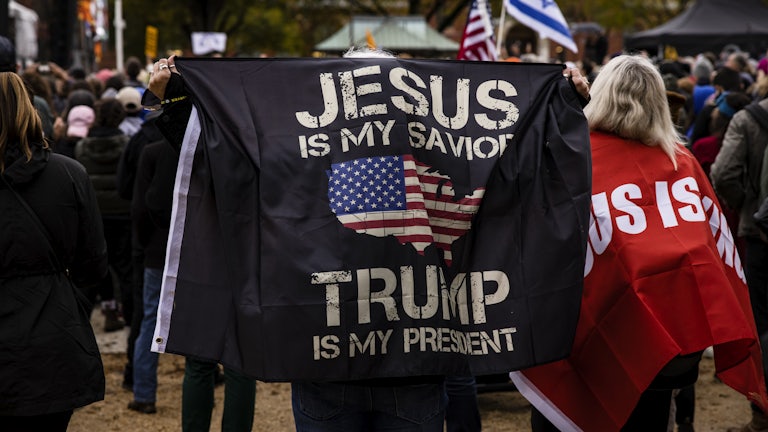 A person holds a banner reading "Jesus is my savior. Trump is my president."
