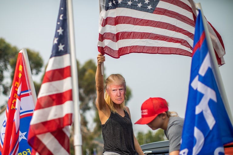 A woman wearing a Trump mask waves an American flag at a rally.