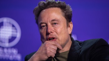 Elon Musk rests his chin on his hand as he speaks