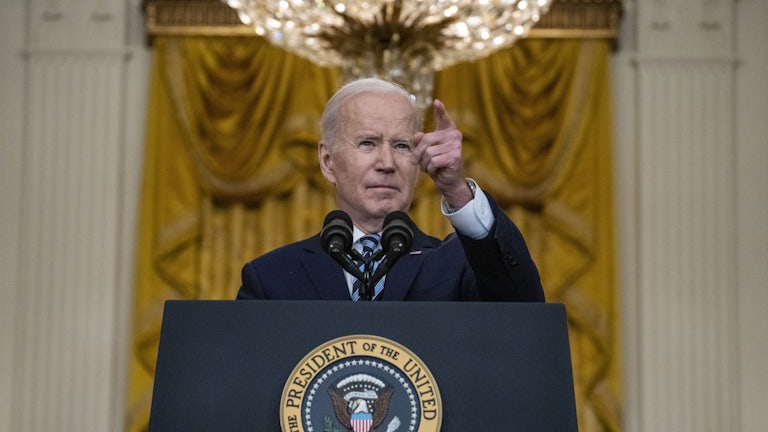 President Joe Biden stands pointing behind a lectern.