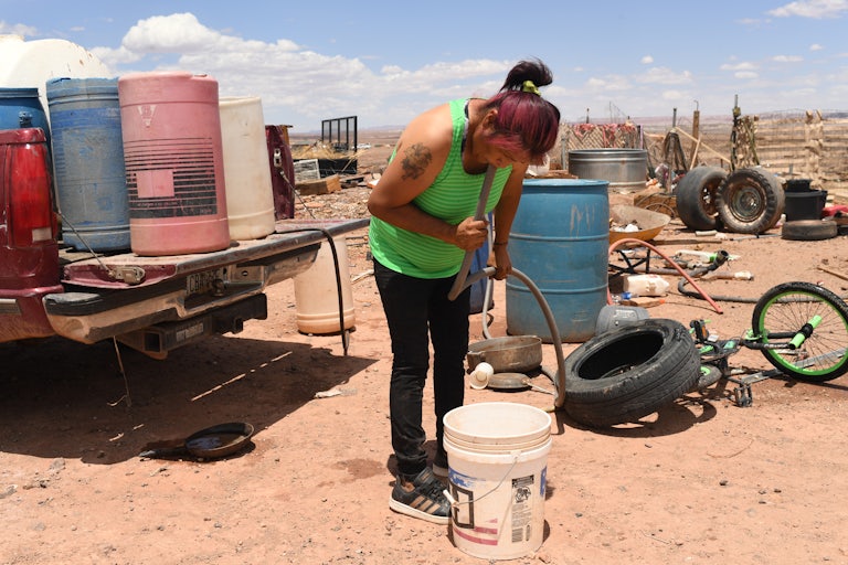 A woman siphons water into a bucket, outside.