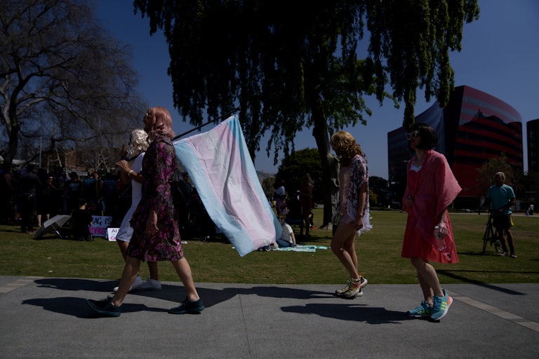 A demonstrator walks down the sidewalk carrying a transgender pride flag