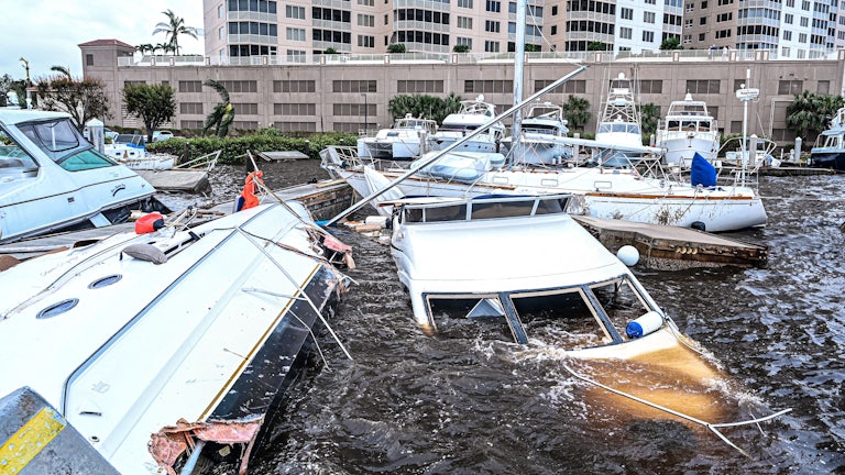 Damaged boats float partially submerged at a marina.