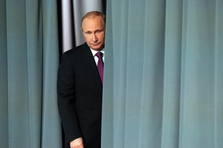 Russian President Vladimir Putin peeks out from behind a grey curtain.