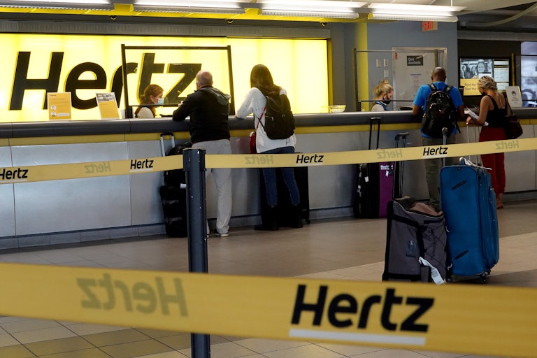 People stand at a Hertz car rental counter in an airport
