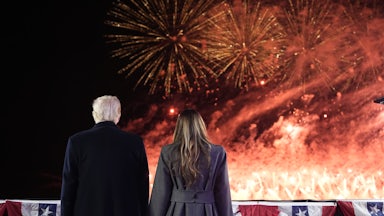 The Trumps hold hands before American flag decorations and a fireworks display that leaves most of the sky awash in flame and smoke.