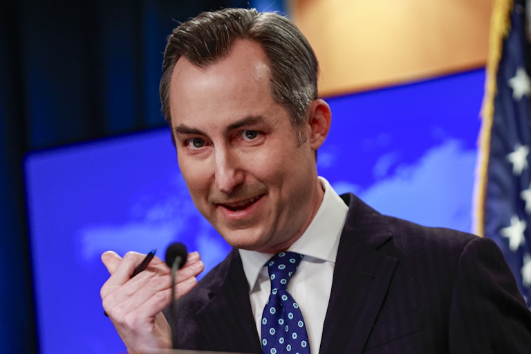 Biden State Department Spokesman Matthew Miller msiles while speaking behind the podium in the briefing room.