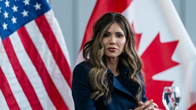 Homeland Security Secretary Kristi Noem sits at a table with her hands folded