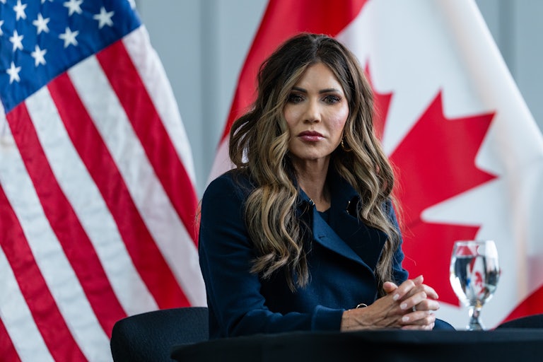 Homeland Security Secretary Kristi Noem sits at a table with her hands folded