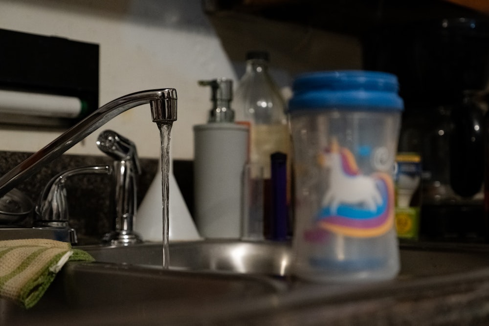 Water comes out of a faucet. A kid's cup with a unicorn on it stands in the foreground.