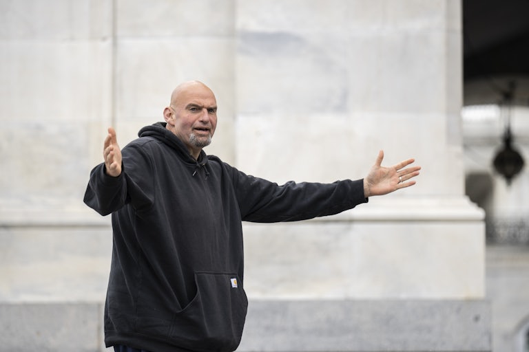 John Fetterman wearing his customary hoodie holds out his arms