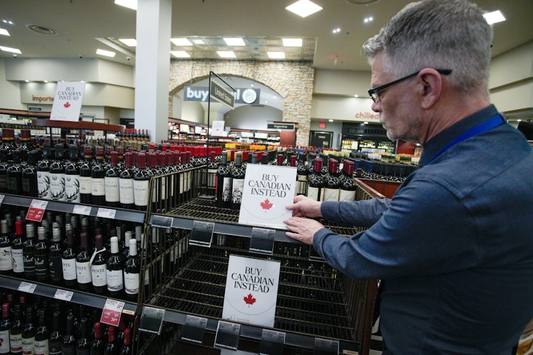 A person puts signs that say, "Buy Canadian instead" on shelves in a liquor store in Vancouver, Canada